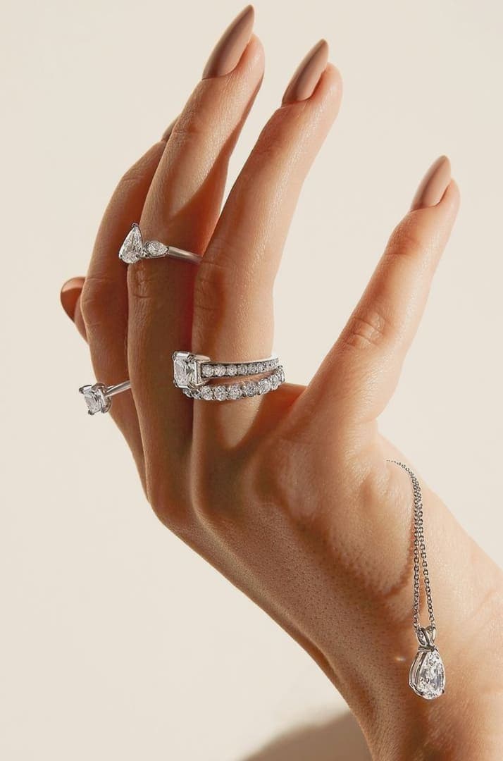 Hand wearing layered rings and a drop necklace